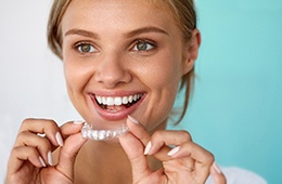 A smiling woman using a teeth whitening tray
